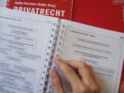 Hand liegt auf aufgeschlagenem Lehrbuch Hand liegt auf aufgeschlagenem Lehrbuch